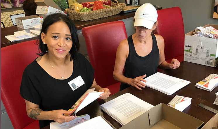 Two women sitting on red chairs sorting through papers